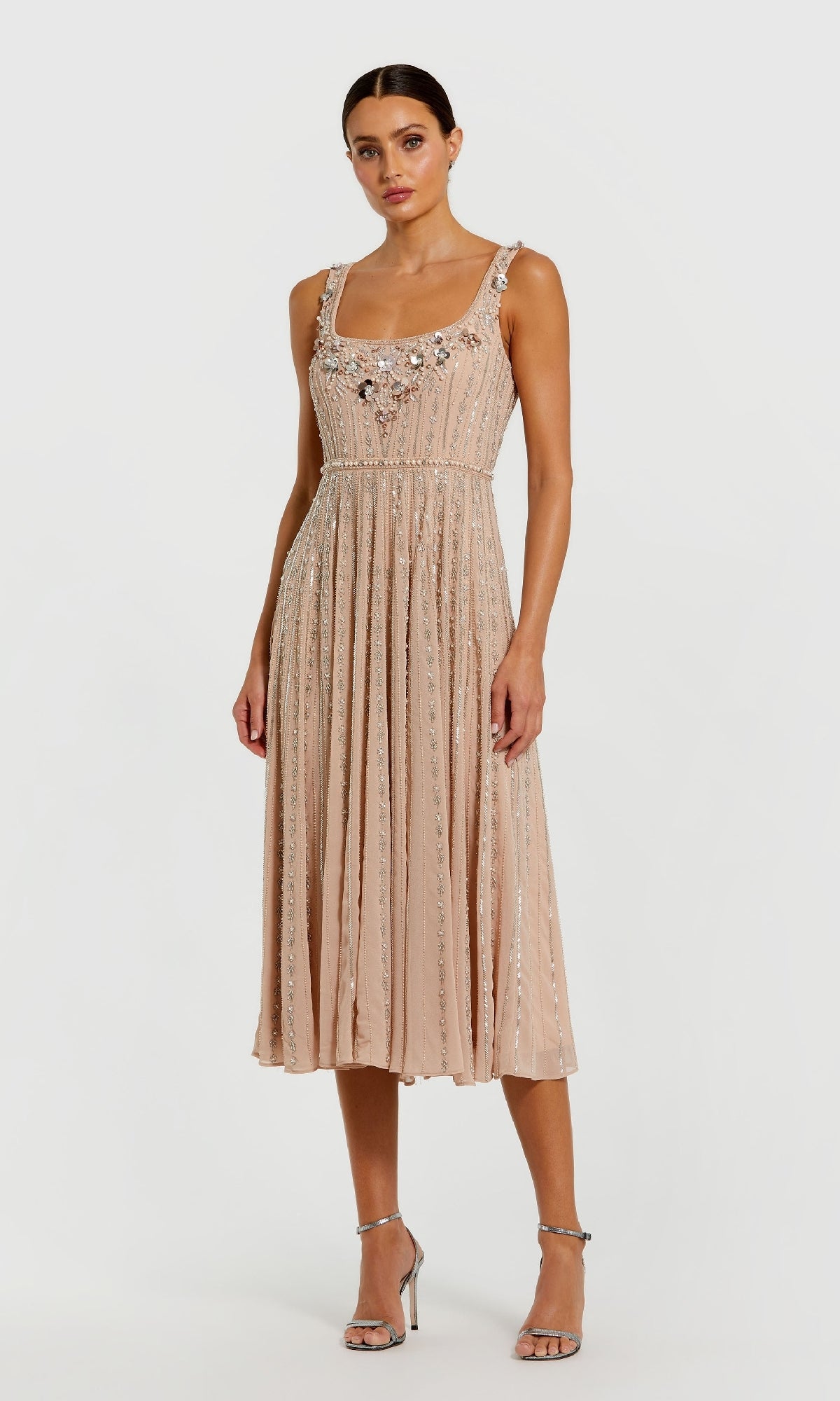 A woman wears the Rose Midi Wedding Guest Dress: Mac Duggal 94155, featuring beaded sequin embellishments, paired with silver high-heeled sandals, standing against a plain white background.